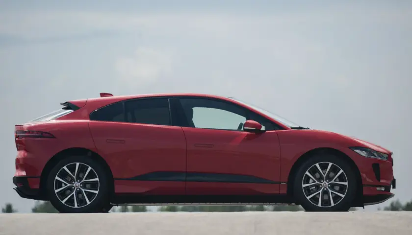 Czerwony jaguar elektryczny z profilu, z widocznymi felgami i linią dachu.