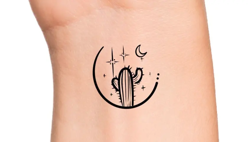 Minimalistyczny kaktus tatuaz na nadgarstku, otoczony księżycem i gwiazdami.