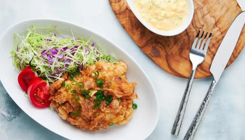Crispy nanban food, a delicious fried chicken dish, served with shredded cabbage, tomato slices, and a creamy tartar sauce.