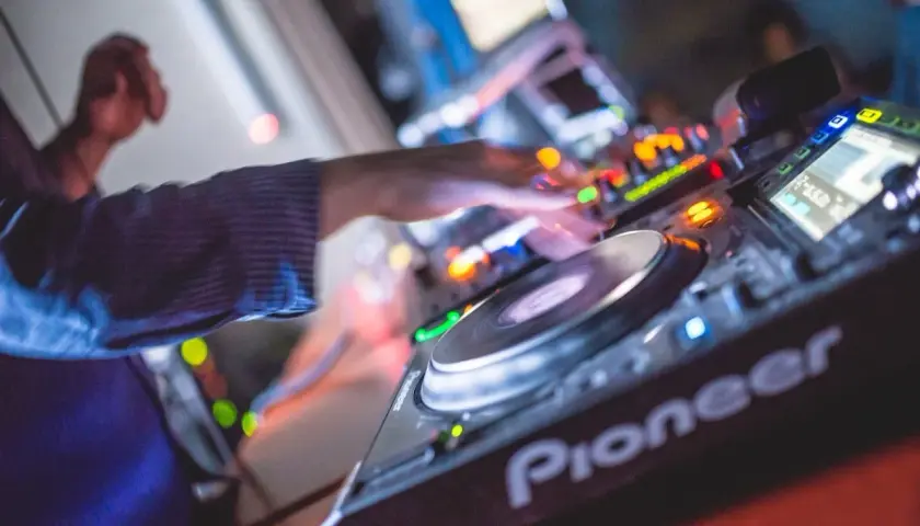 Les mains d'un DJ mixent sur une platine Pioneer, là où les DJs trouvent leur musique. Lumières colorées et ambiance festive.