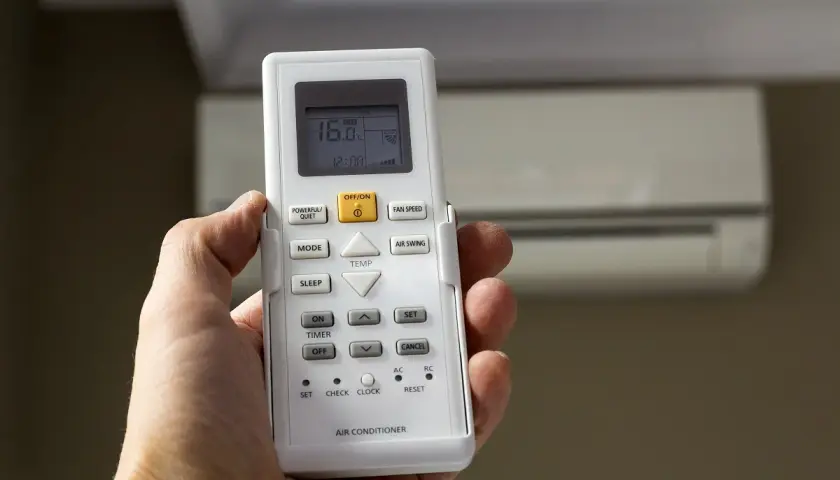 Mano sujetando control remoto de aire acondicionado, mostrando 16°C. La "A" en el aire acondicionado podría indicar modo automático o alguna función específica.