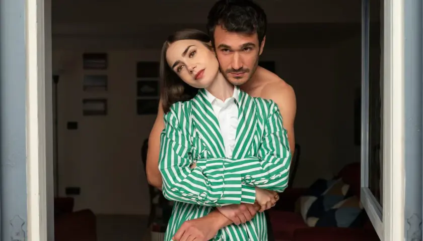 Emily w Paryżu przytulona do ukochanego. Ona w zielono-białej marynarce, on bez koszulki.