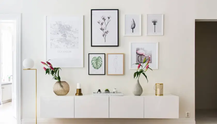 Ett modernt, vitt sideboard med konstverk ovanför, inklusive en Stockholmskarta och en flamingo. En golvlampa och vaser ger en stilfull touch.