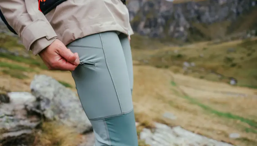 Dłoń zamyka zamek w kieszeni, pokazując jakie spodnie trekkingowe są idealne na górskie wędrówki.