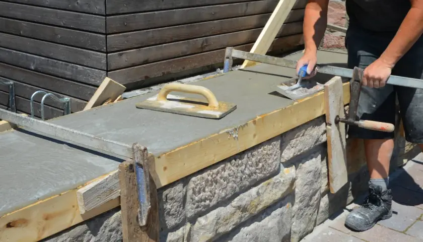 Arbeiter glättet frischen Beton auf einer **Wandschalung**. Der Aufbau der Schalung aus Holz und Metall ist gut sichtbar.