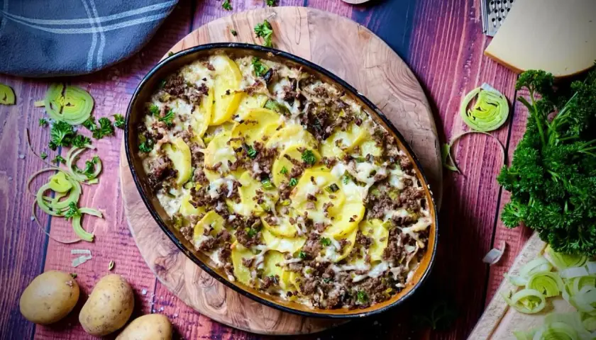 Herzhafter kartoffelauflauf aus rohen Kartoffeln mit Hackfleisch, überbacken mit Käse. Garniert mit Petersilie und Lauch.