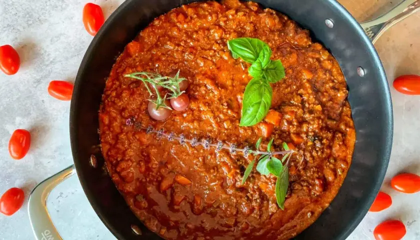 Herzhafte rotwein bolognese in einer Pfanne, garniert mit Basilikum und Kirschtomaten.