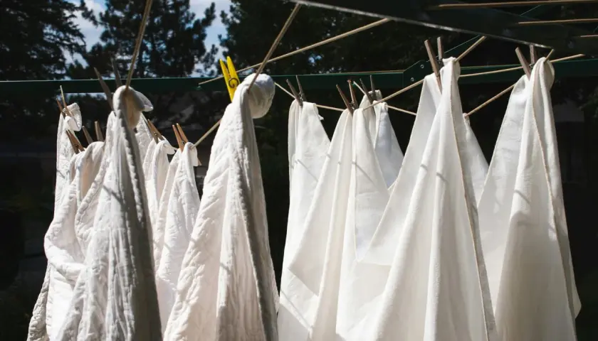 Des linges blancs, dont un pantalon, sèchent au soleil. Une astuce pour savoir comment blanchir un pantalon blanc : le laisser sécher à l'air libre après un bon lavage.