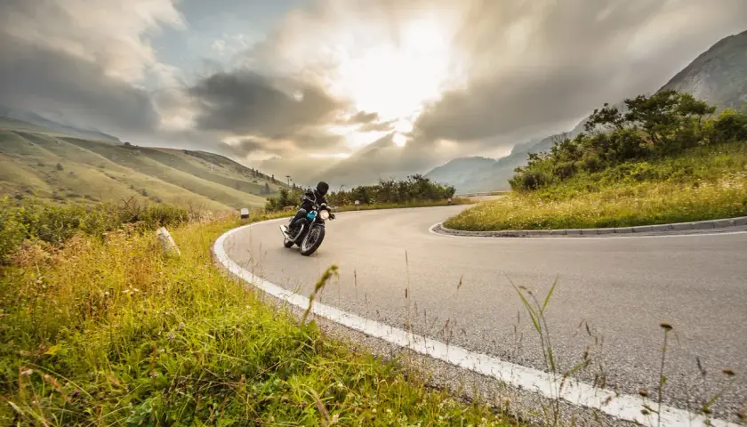 Un motociclista affronta una curva su una strada di montagna, godendosi un perfetto weekend in moto tra paesaggi mozzafiato e cielo nuvoloso.