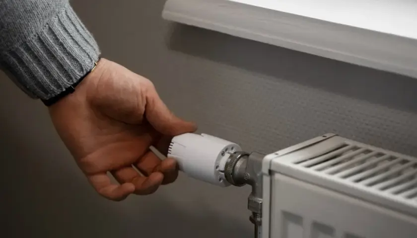Dłoń reguluje termostat grzejnika, kontrolując, ile wynosi ogrzewanie gazowe.