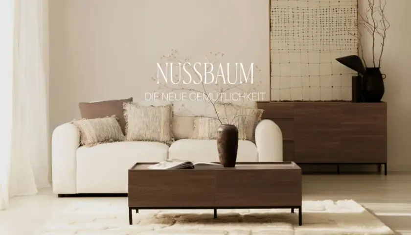 Gemütliches Wohnzimmer mit weißem Sofa, Kissen und einem Couchtisch aus dunklem Holz. Ein Sideboard aus dunklem Holz steht im Hintergrund.