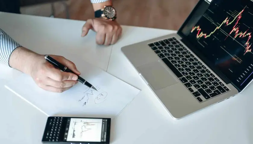 Analiza wykresów na laptopie i telefonie, notatki na papierze. To może być przygotowanie do gry na giełdzie, jak na stooq.