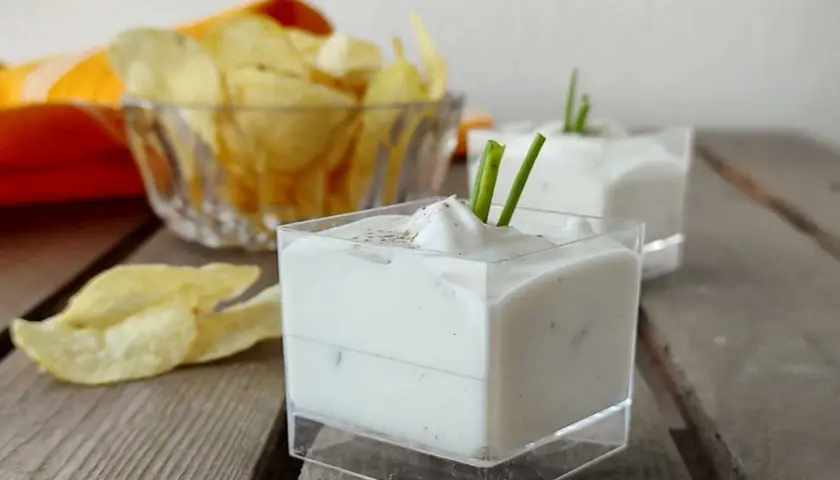Salsa yogurt cremosa, guarnita con erba cipollina, pronta per accompagnare patatine croccanti.