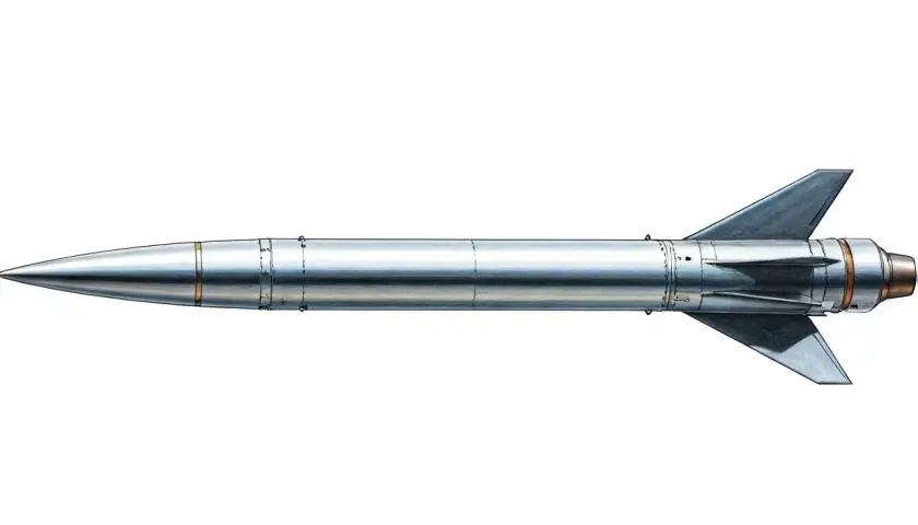 Srebrzysta rakieta, czyli missile po polsku, z ostrym stożkiem i trójkątnymi stabilizatorami, gotowa do startu.