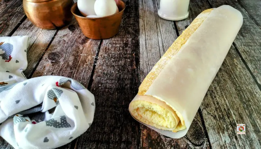 Rotolo di pasta biscotto perfetta, soffice e dorata, avvolta in carta forno. Ingredienti freschi in primo piano.