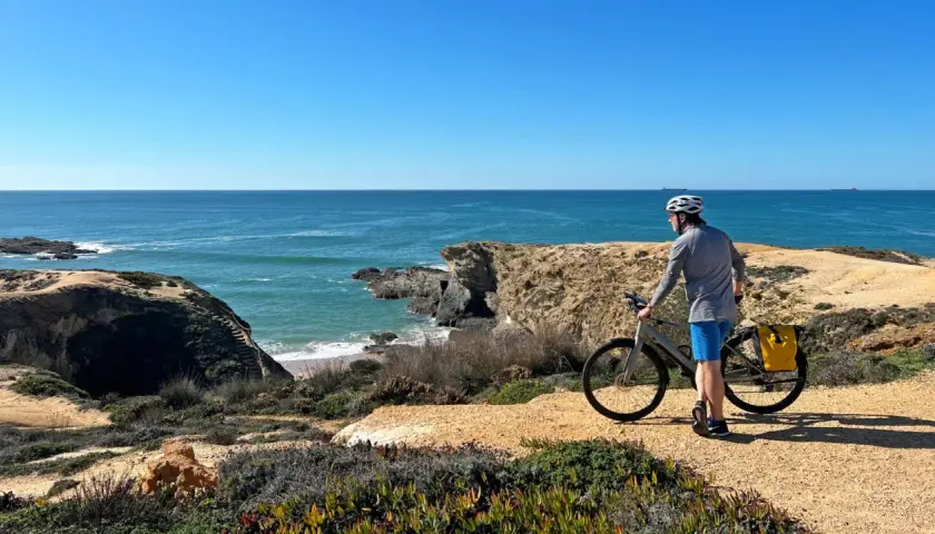 A cyclist pauses on a cliffside path during a Porto to Lisbon bike tour, admiring the vast blue ocean.