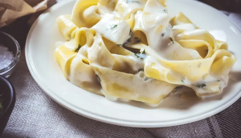Makaron tagliatelle w kremowym sosie serowym z ziołami na białym talerzu.
