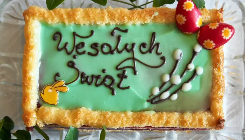 Zielone ciasto wielkanocne z napisem "Wesołych Świąt", ozdobione zajączkiem, baziami i pisankami.