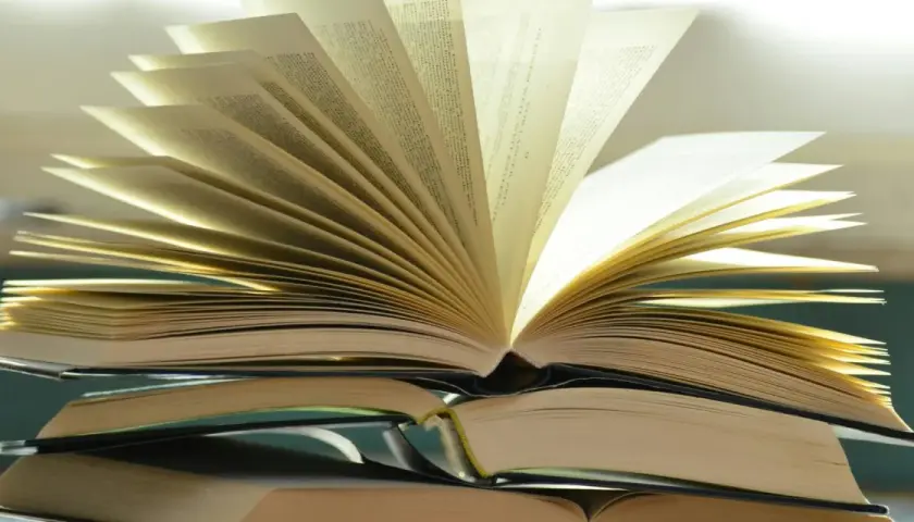 Otwarta książka na stosie innych. Różnica między romansem a literaturą obyczajową z wątkiem miłosnym jest jak między stronami tej książki – subtelna, lecz znacząca.