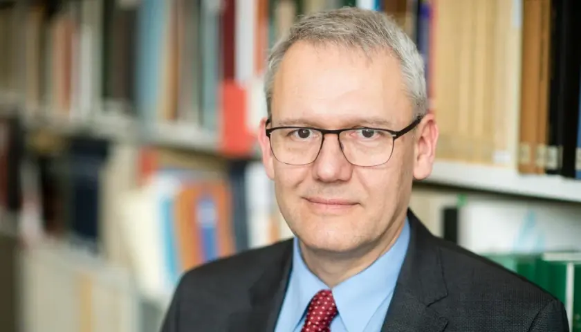 Porträt von Andreas Wirsching, der in einem Anzug und mit Brille vor einem Bücherregal steht.