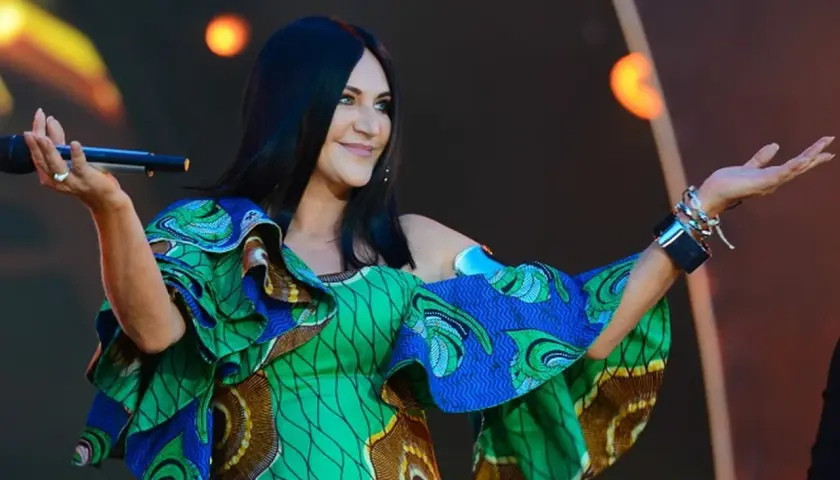 Kayah w kolorowej sukience z falbanami śpiewa na scenie, trzymając mikrofon.