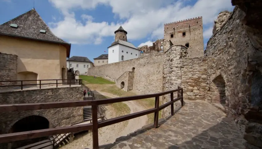 Kamienne mury i wieże zamku Stará Ľubovňa wznoszą się na tle błękitnego nieba z chmurami.
