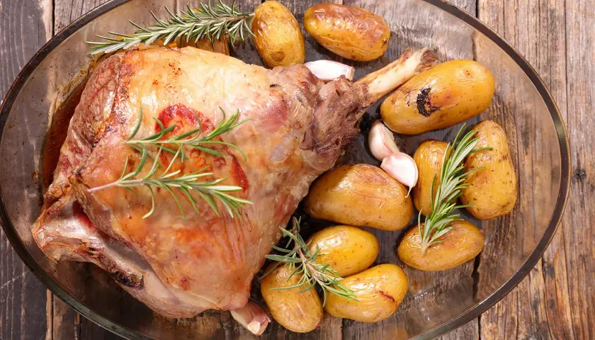 Gigot d'agneau rôti, doré et savoureux, accompagné de pommes de terre grenaille et d'ail, prêt pour la cuisson.