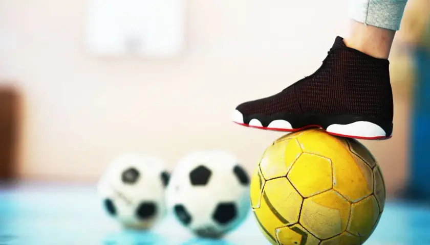 Stopa na żółtej piłce, w tle dwie białe. To pytanie: futsal co to?
