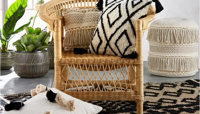 A rattan chair with decorative pillows and a fringed pouf, showcasing various types of fancy chairs and bohemian decor.