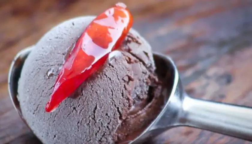 Un cucchiaio di gelato al cioccolato con una decorazione di peperoncino rosso lucido. Un'esplosione di dolcezza e piccantezza.