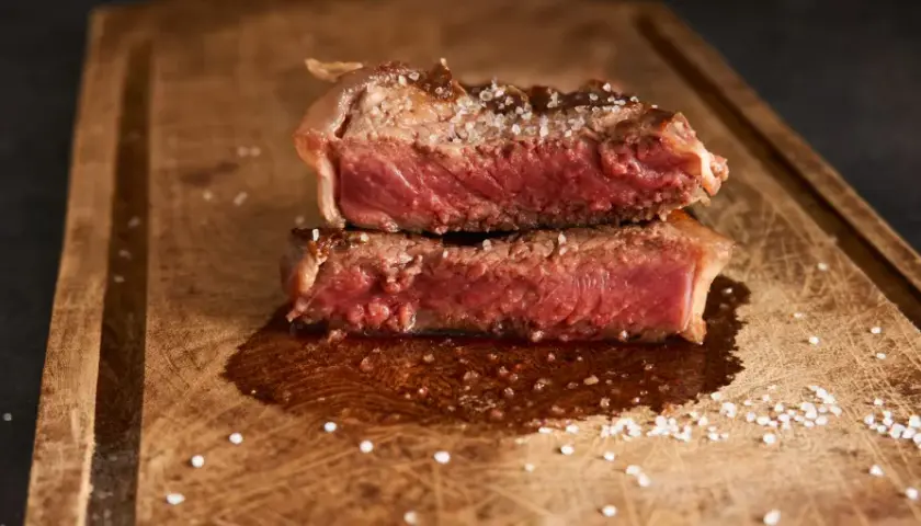 Filet mignon coupé en deux, saignant et parsemé de gros sel sur une planche en bois. Parfait pour une recette filet mignon moelleux.