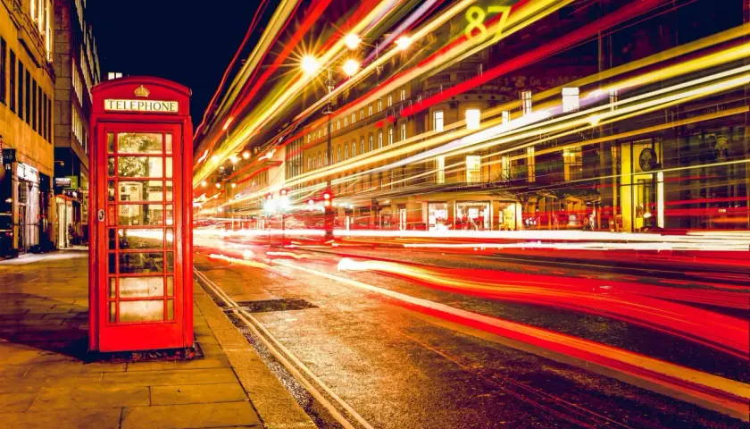 Klasyczna czerwona budka telefoniczna na tle nocnej ulicy z rozmazanymi światłami samochodów, efekt długi czas naswietlania zdjecia.
