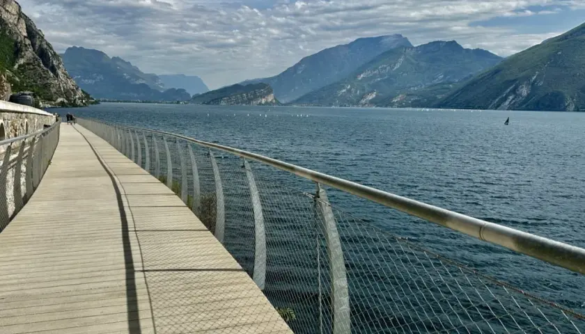 Drewniana promenada nad jeziorem Garda, z widokiem na góry i żaglówki. Idealne miejsce na spacer po mieście.