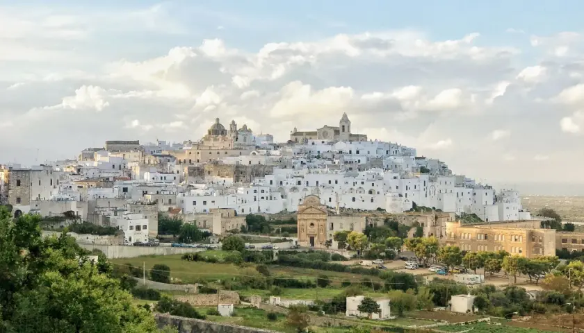 A white city perched on a hill, reminiscent of a scene from Puglia, Italy, with a church and scattered buildings.