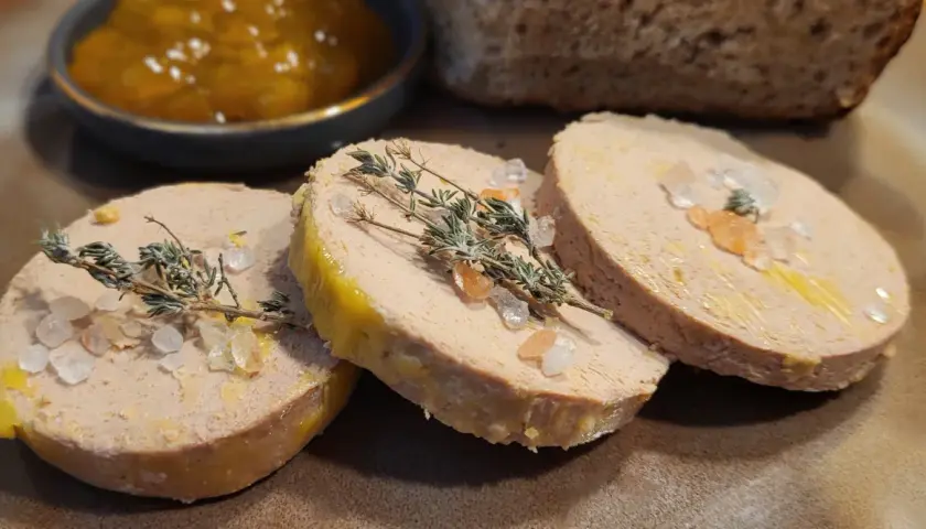 Trzy plastry foie gras, posypane solą i gałązkami tymianku, obok dżemu i chleba. Foie gras co to? Delikatesowy pasztet z gęsiej lub kaczej wątróbki.