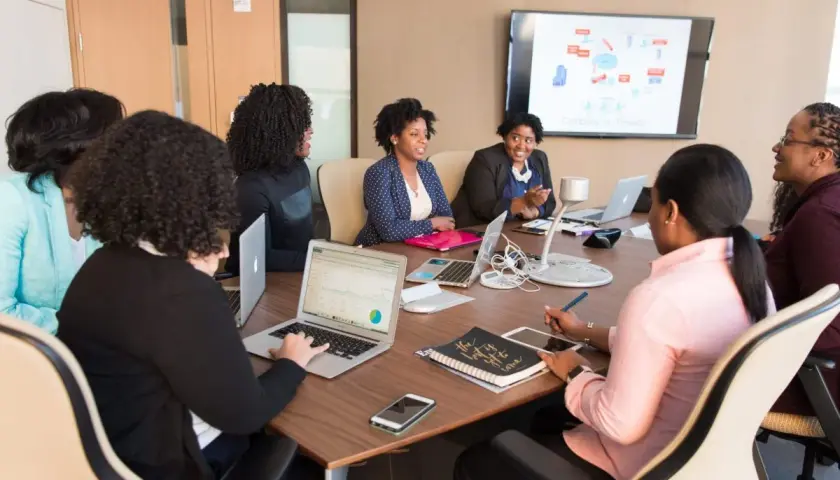 A diverse team collaborates in a meeting room, with one woman acting as an internal coach, guiding the discussion.