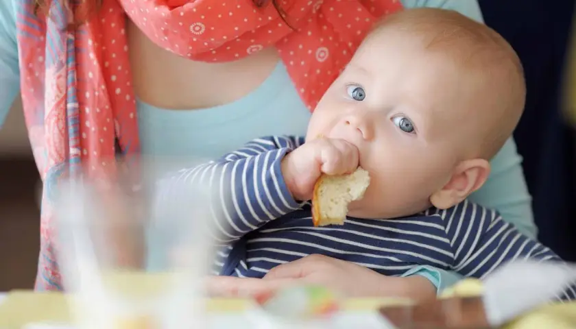 Bambino con occhi azzurri assaggia un pezzo di pane, un momento chiave per capire quando iniziare lo svezzamento.