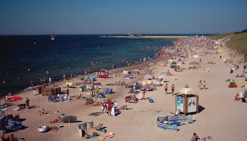 Tłum ludzi wypoczywa na plaży w Darłówku. Słońce, morze i piasek tworzą idealne warunki do relaksu.