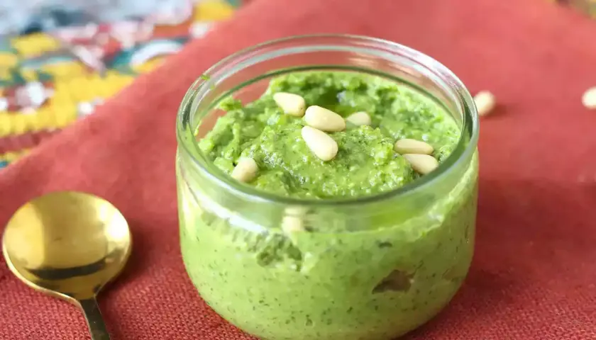 Un frasco de pesto casero, perfecto para tu próxima pasta al pesto receta, adornado con piñones.
