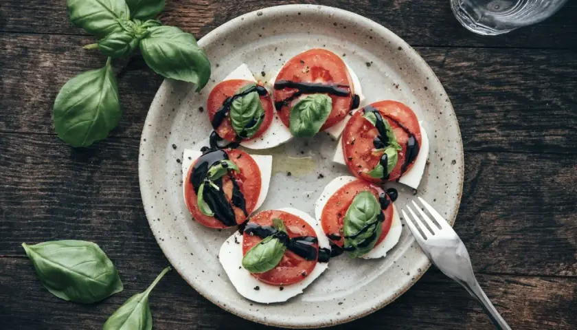 Tomate-Mozzarella-Salat mit frischem Basilikum und Balsamico-Glasur auf einem rustikalen Teller.