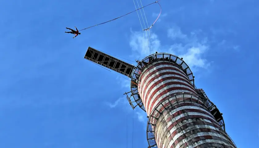 Osoba skacze na bungee z wieży, doświadczając adrenaliny. To najwyższe bungee w Polsce, oferujące niezapomniane wrażenia.