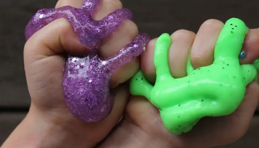 Dzieci bawią się fioletowym i zielonym slime'em, pokazując, jak zrobić slime.