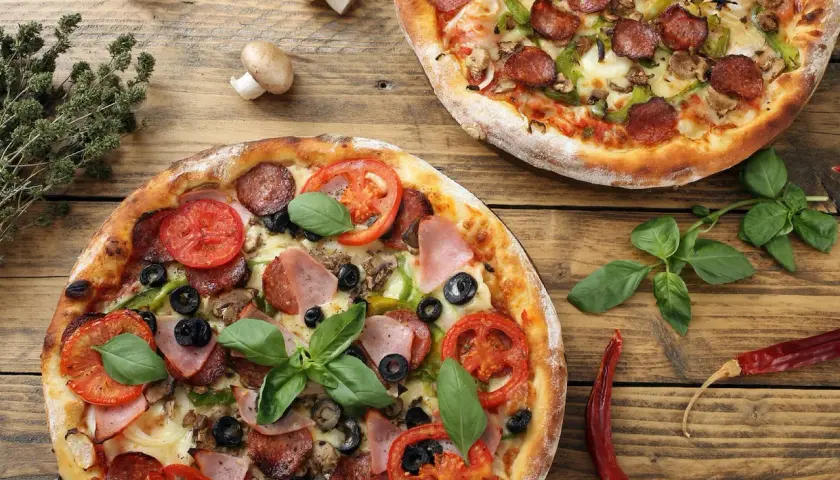 Dwie pizze z różnymi dodatkami: jedna z salami, papryką i pieczarkami, druga z szynką, pomidorami i oliwkami. Idealne na wspólne jedzenie, pokazujące jakie dodatki do pizzy wybrać.
