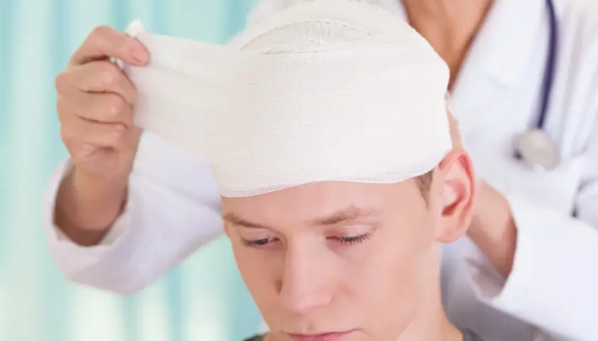 Lekarz opatruje głowę młodego mężczyzny, który doznał urazu aksonalnego.