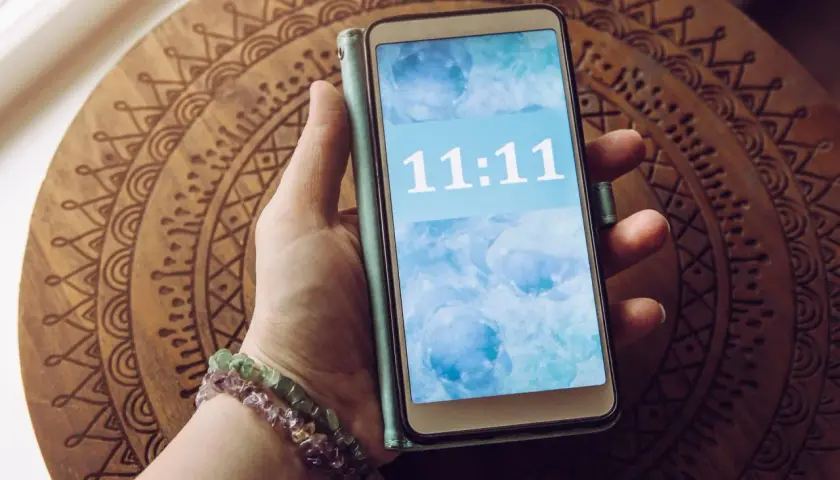Dłoń z bransoletkami trzyma telefon z wyświetloną godziną 11:11. To znak, że 11.11 znaczenie ma dla wielu osób.