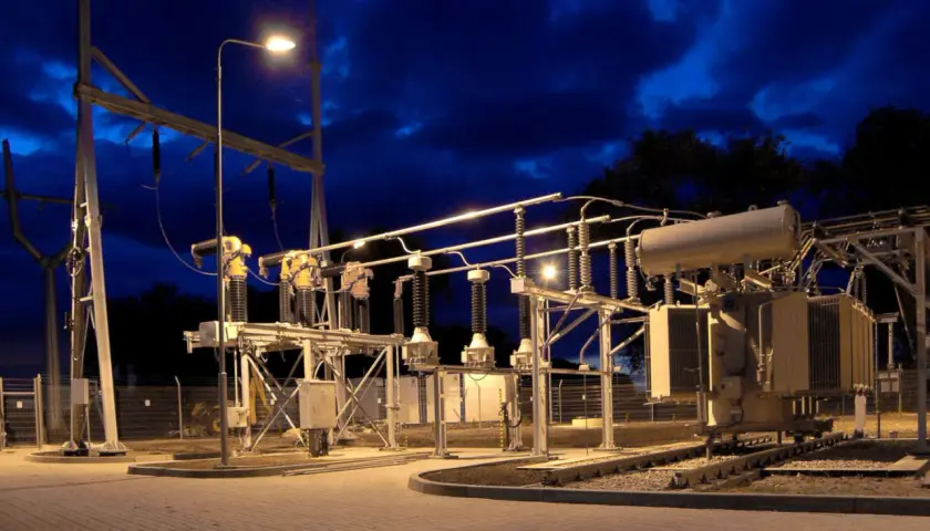 Nocna iluminacja podstacji trakcyjnej z transformatorem i izolatorami.