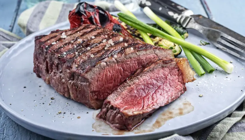 Un pavé de rumsteak grillé, coupé en tranches, servi avec des légumes rôtis et des oignons verts.
