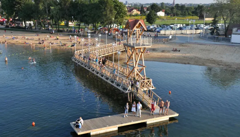 Ludzie odpoczywają na plaży i w wodzie przy drewnianym molo w Pogorii, Dąbrowa Górnicza.