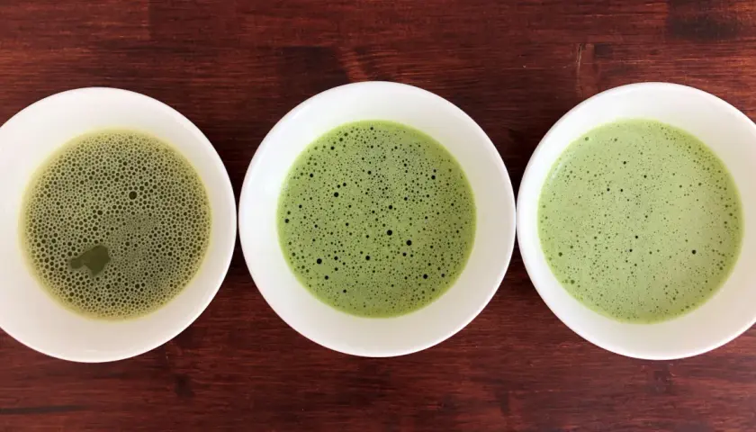 Drei Schalen mit schaumigem Matcha in verschiedenen Grüntönen, von hellgrün bis tiefgrün.