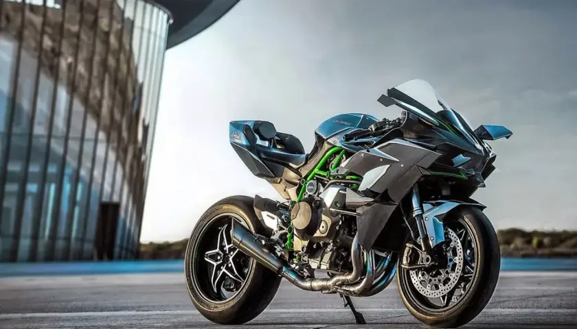Czarny Kawasaki Ninja H2R, znany jako najszybszy motor na świecie, z zielonymi akcentami, stoi przed nowoczesnym budynkiem.